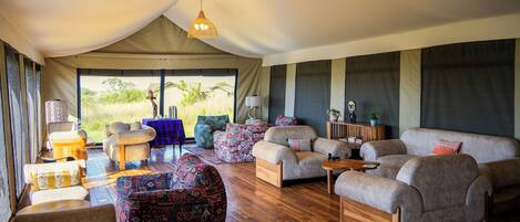 A spacious tented room with a wooden floor, multiple seating areas including sofas and chairs, and hanging woven light fixtures.