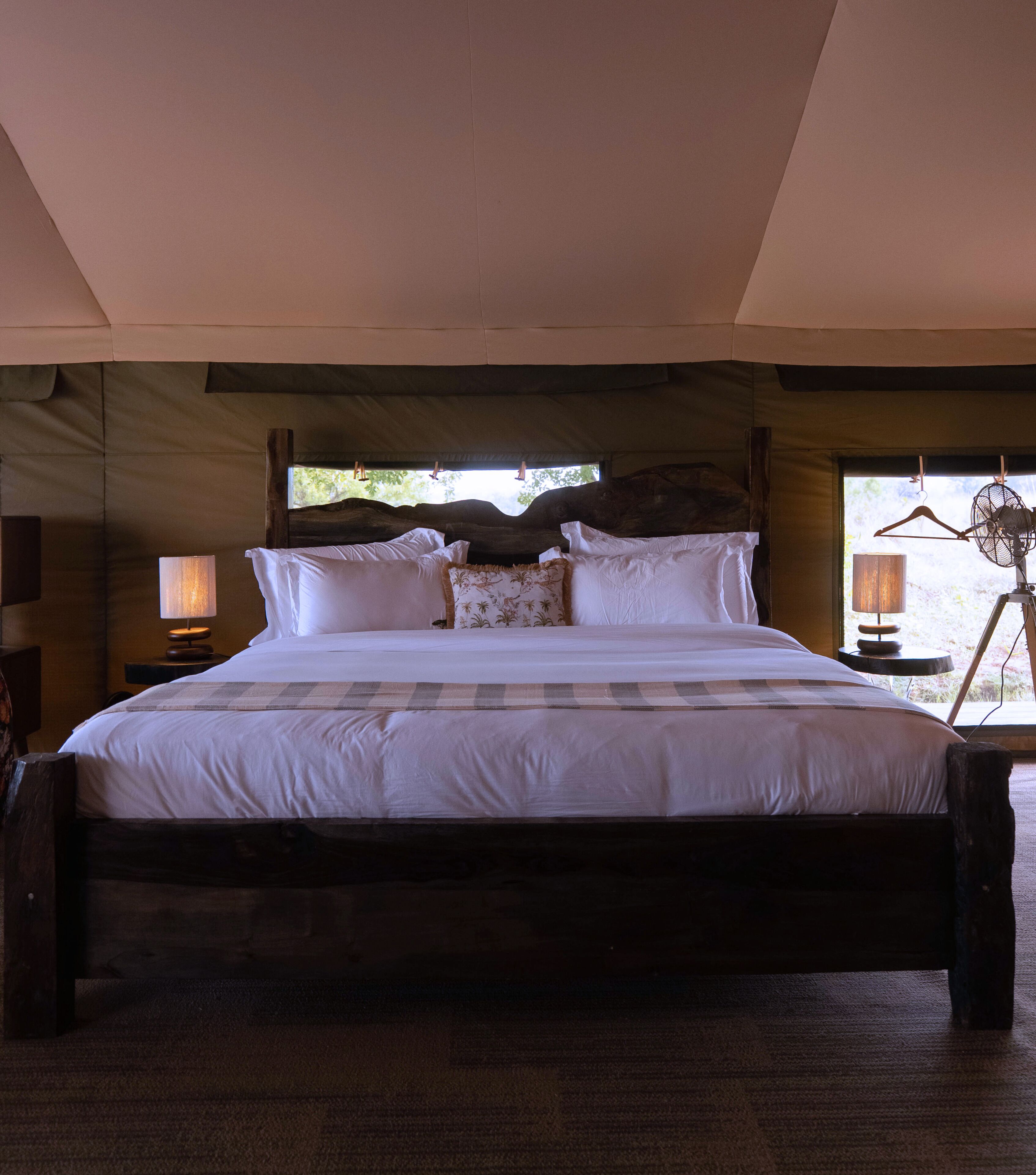 A large bed with white linens and multiple pillows, a wooden headboard, and a hanging fan.