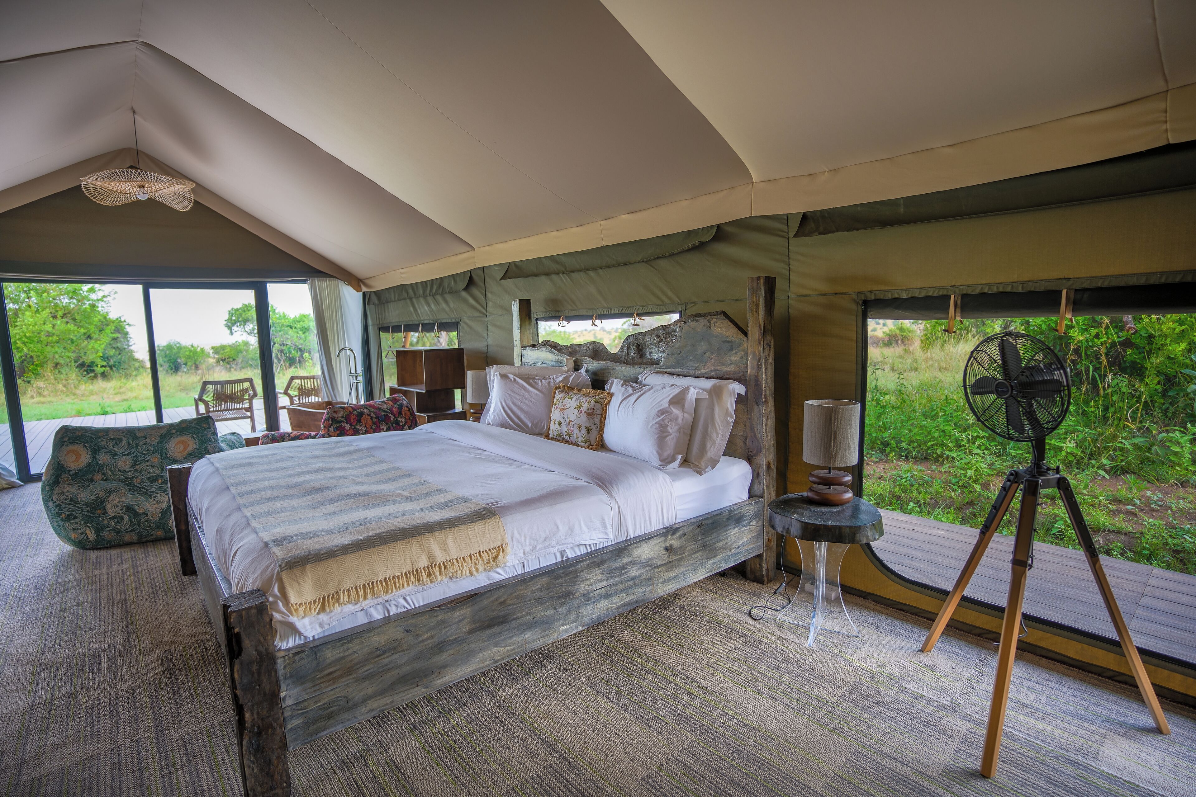 Amplia habitación con toldo, una cama grande, un ventilador y vistas al exterior.