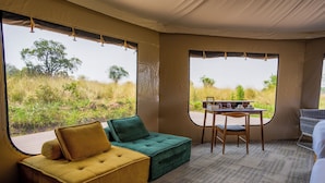 Una habitación con sofá, una mesa y sillas, ventanas amplias con vistas al exterior.