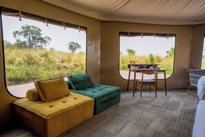 A room with a sofa, a table, and chairs, large windows with a view of the outdoors. - Malaika Mara River Luxury Camp (Serengeti)