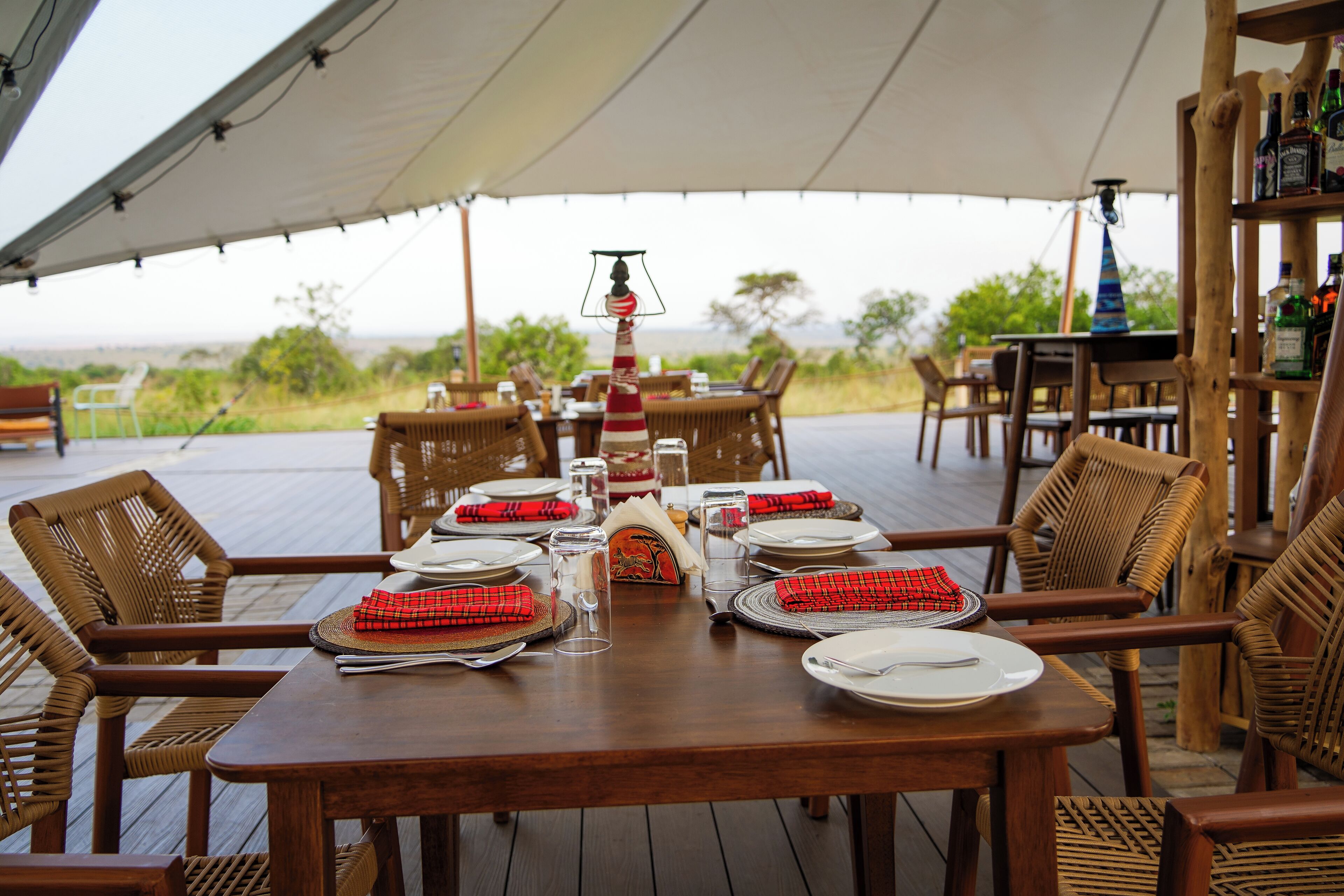A dining area with wooden tables and chairs, set for a meal with red napkins and glassware.