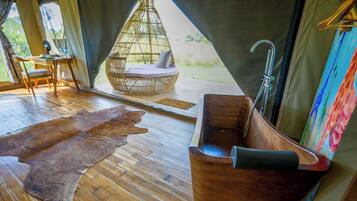 A wooden floor, a wooden bathtub, a woven hanging chair, and a fur rug.