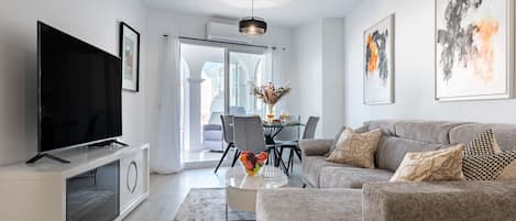A modern living room with a flat-screen TV, grey sofa, and artwork on the walls.