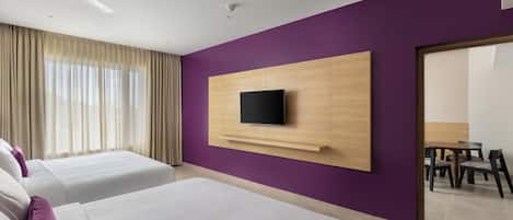 A hotel room with two beds, a TV mounted on a wooden panel, a ceiling fan, and a view of a dining area through a glass door.