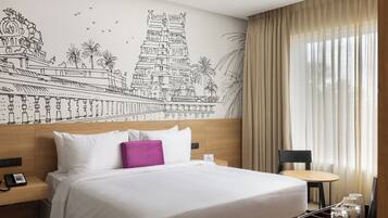 A hotel room with a large bed, a nightstand, a desk, and a chair. There is a mural on the wall depicting a temple and palm trees.