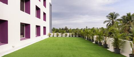 A building with a white facade and purple accents, a green lawn, and rows of potted plants.