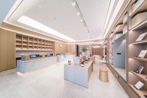 A modern hotel lobby with a reception desk, seating area, and shelves with informational materials. - Ji Hotel Shenzhen Baoan Pingzhou Subway Station (Shenzhen)