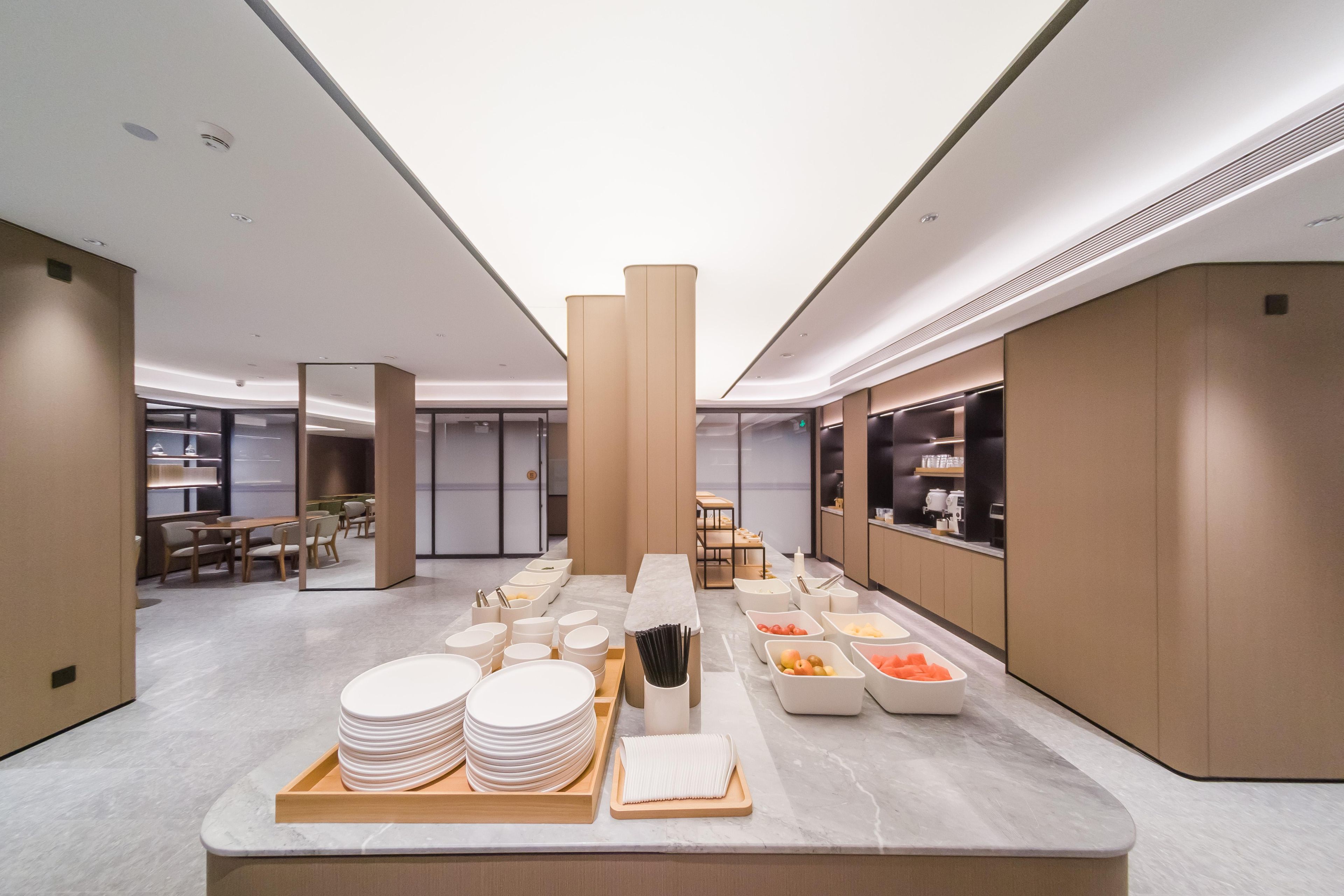 A modern hotel lobby with a buffet area featuring plates, bowls, and a fruit tray.
