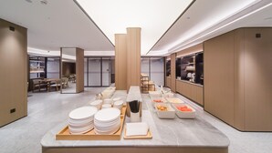 A modern hotel lobby with a buffet area featuring plates, bowls, and a fruit tray. - Ji Hotel Shenzhen Baoan Pingzhou Subway Station (Shenzhen)