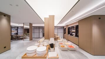 A modern hotel lobby with a buffet area featuring plates, bowls, and a fruit tray.