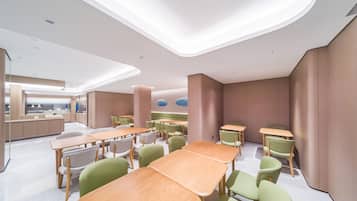 Un comedor moderno con varias mesas y sillas, iluminación empotrada en el techo y vistas al área de la cocina de fondo.