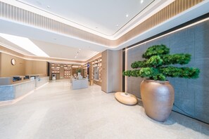 Un hall d’hôtel moderne avec un comptoir d’accueil, une grande plante en pot et un écran fixé au mur.