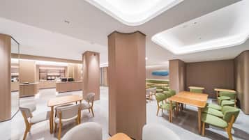 Un interior moderno con una columna central, mesas, sillas y una zona de cocina al fondo.