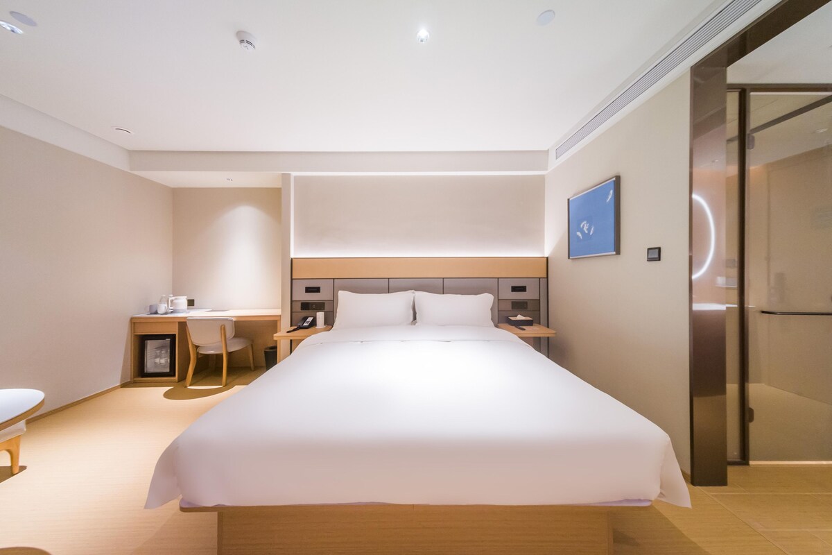 A modern hotel room with a large bed, bedside tables, a desk, and a chair.