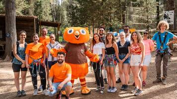 A group of people in an outdoor setting with a mascot, surrounded by trees and a wooden structure.