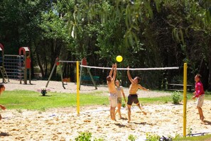 Partido de voleibol de playa con jugadores en movimiento, una red y una cancha de arena.