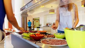 Un buffet avec différents plats présentés dans des bols, une personne qui sert les plats et une autre personne en arrière-plan.