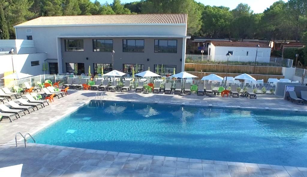Ein Schwimmbecken mit Liegestühlen und Sonnenschirmen, ein modernes Gebäude mit großen Fenstern und ein klarer Himmel.