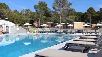 Une piscine entourée d’arbres et de bâtiments, avec des chaises longues et des parasols.