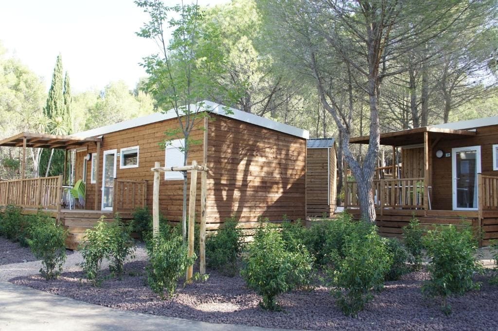 Eine Holzhütte mit einer Terrasse, umgeben von Sträuchern und Bäumen.