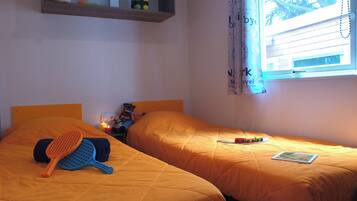 Ein Zimmer mit zwei Betten, einer Ablage mit Gegenständen, einem Fenster mit Vorhängen und einem kleinen Tisch mit einem Spielzeug.