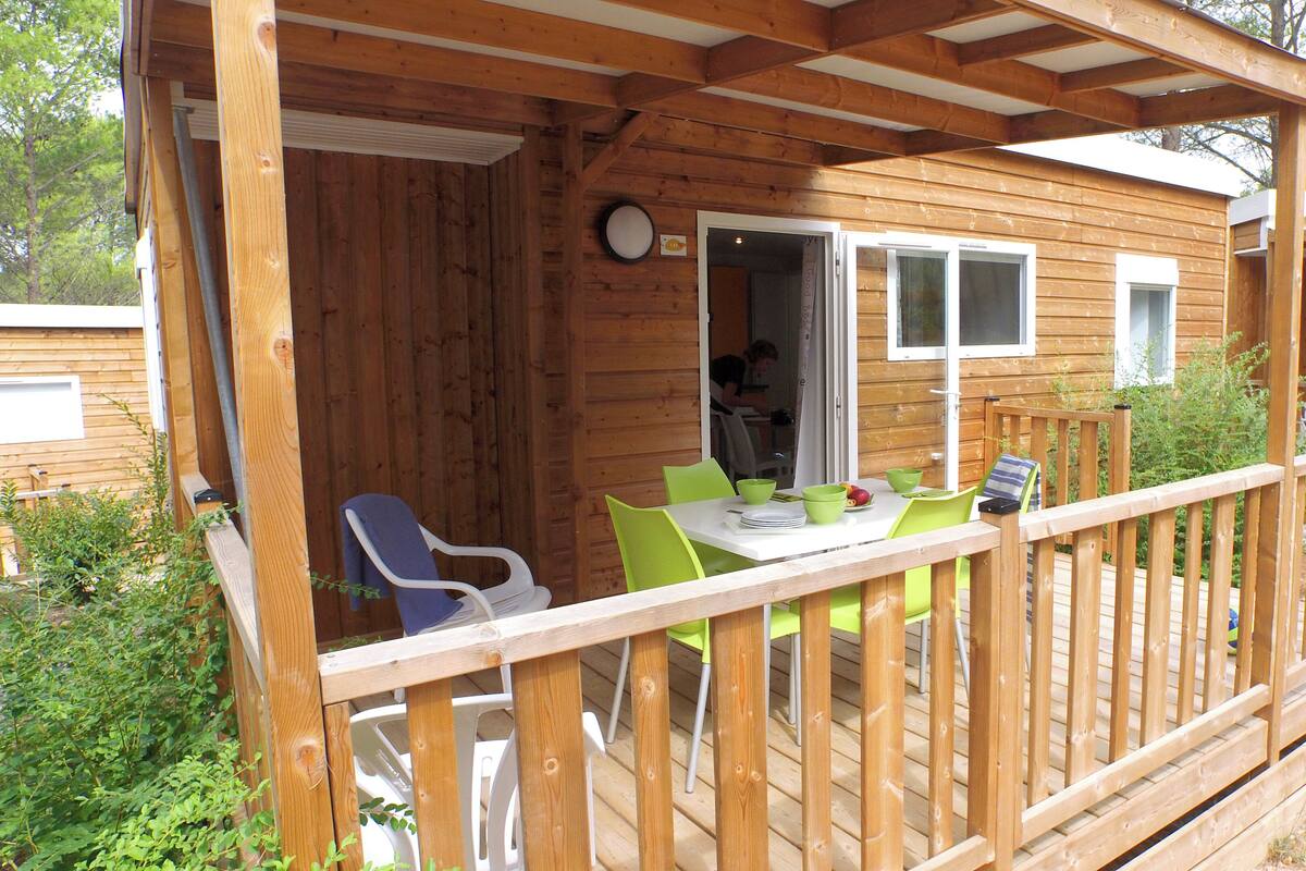 Um deck de madeira com mesa, cadeiras, uma janela e uma porta que dá para o interior.