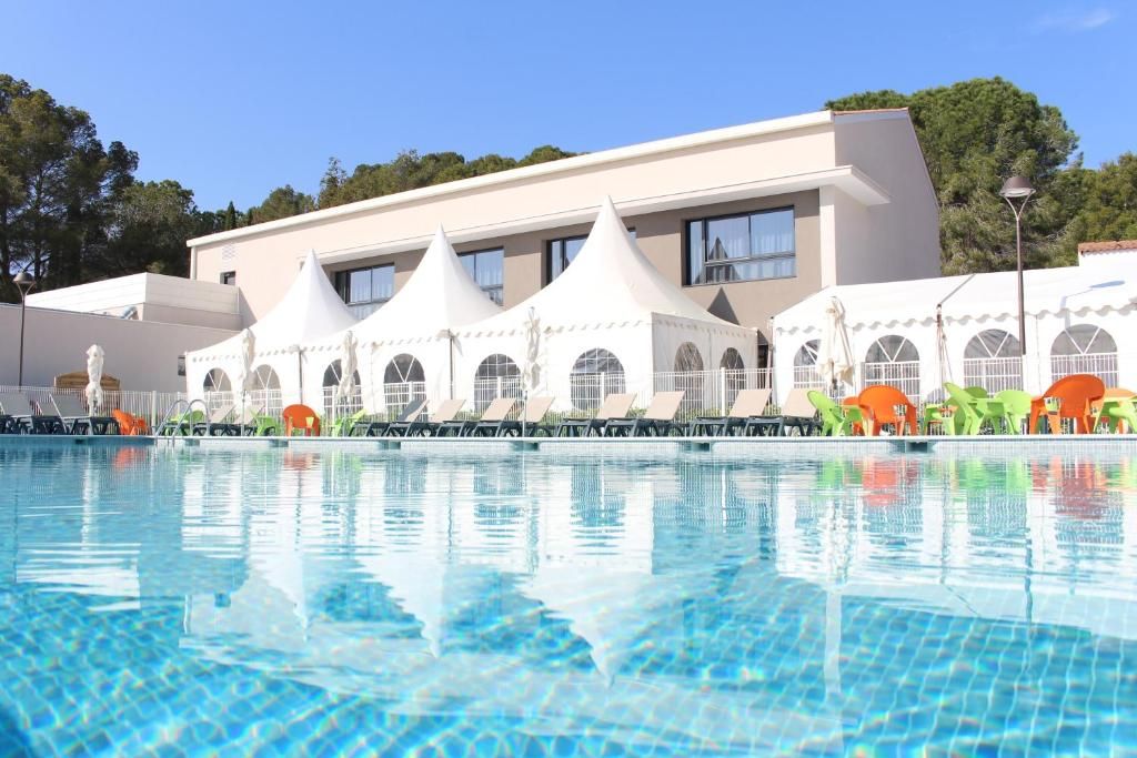 Une piscine avec des chaises longues et un bâtiment doté de nombreuses fenêtres et d’une façade blanche.