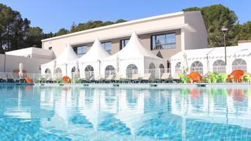 Une piscine avec des chaises longues et un bâtiment doté de nombreuses fenêtres et d’une façade blanche.