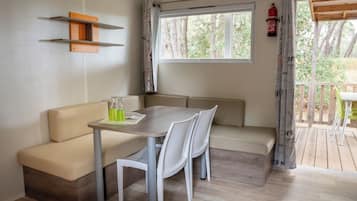 Une pièce chaleureuse avec un plancher en bois, un canapé beige, une petite table avec des chaises, une fenêtre avec des rideaux et un extincteur accroché au mur.