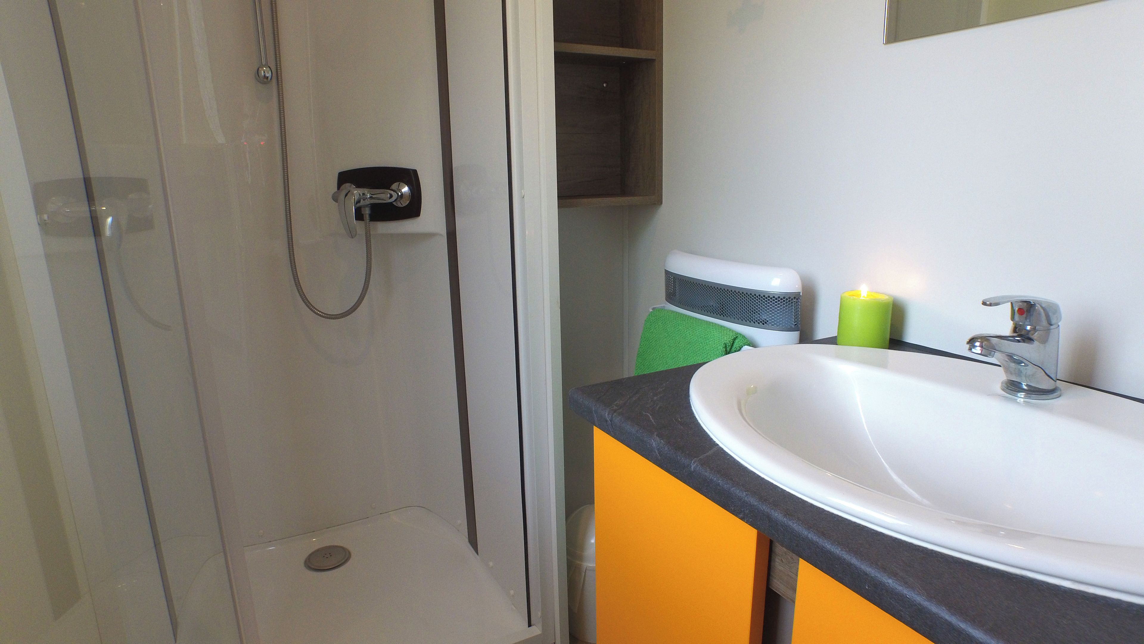 A bathroom with a shower, a sink, and a green candle on the counter.