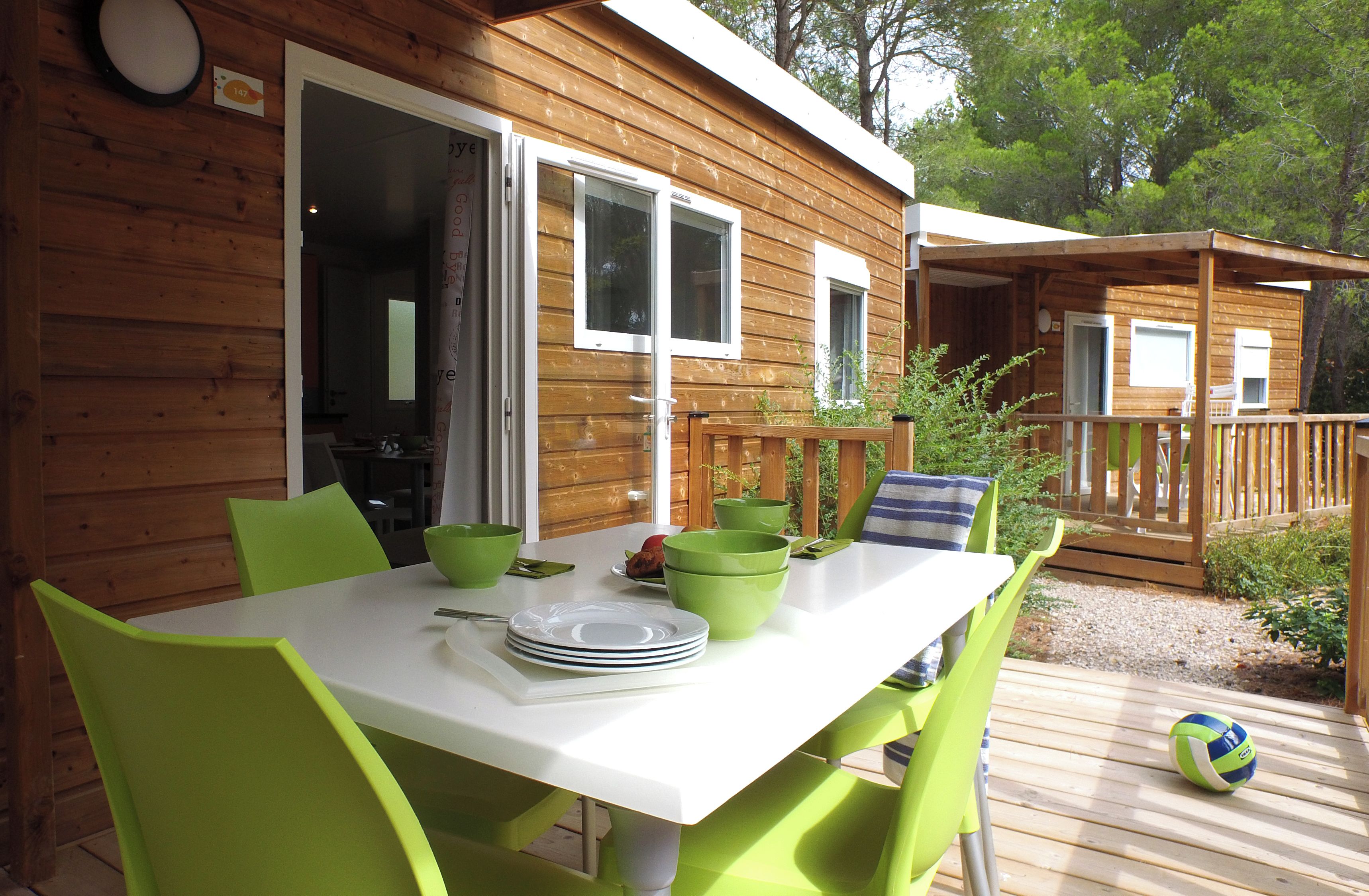 A wooden cabin with a dining table and chairs, a volleyball, and a deck.