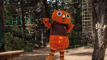 A mascot in a forested area with rope bridges and a wooden bench.