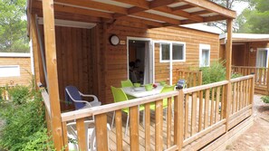 Una terraza de madera con una mesa, sillas, un ventanal y una puerta que da a un espacio interior.