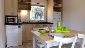 A compact kitchen with a microwave, coffee maker, and a small dishwasher. There's a dining table with chairs and a window above the sink.
