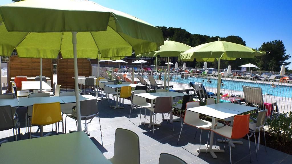 An outdoor pool area with tables and chairs, umbrellas, and a view of the pool.