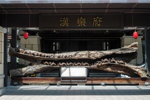 A building entrance with a large wooden sculpture and a sign with Chinese characters. - Xi'an Paradise Hotel of Han Dynasty (Xi'an)