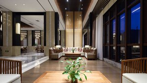 Un vestíbulo moderno con área de descanso central, ventanas amplias y una planta decorativa.