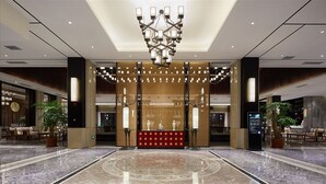 Un amplio vestíbulo con candelabro, una zona de estar roja y un gran panel de pared de madera.