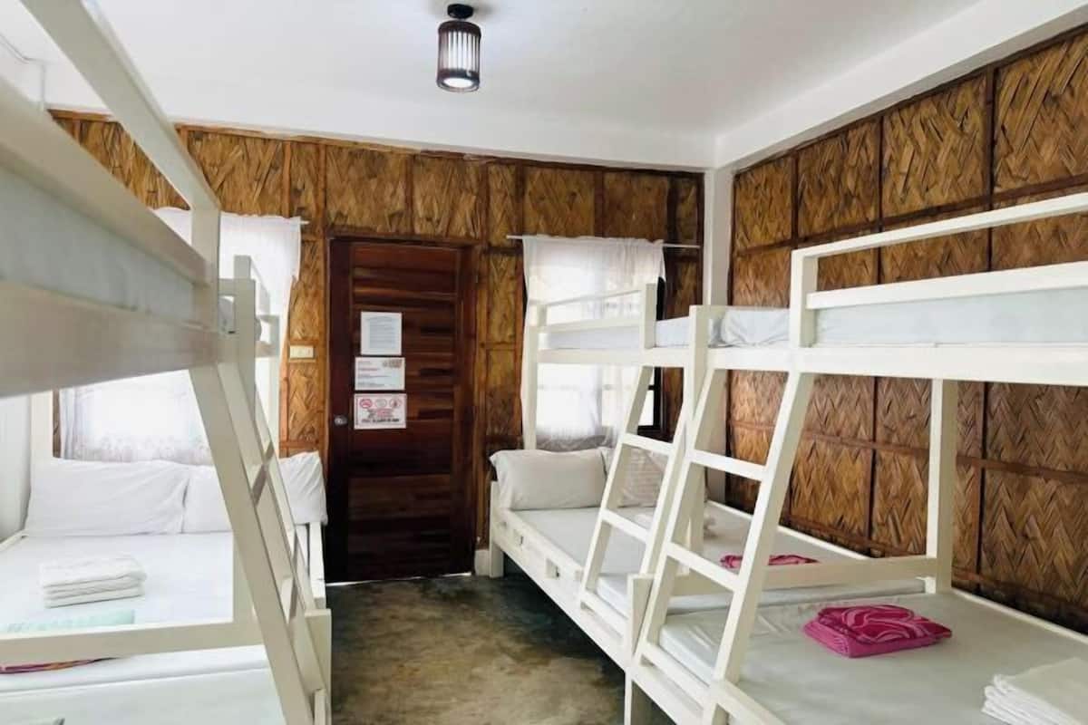 Een kamer met stapelbedden, houten wandpanelen, een deur en een klein raam met gordijnen.