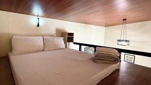 A bedroom with a wooden ceiling, a bed with white linens, a bedside lamp, and a small artwork on the wall. - Camp Saint John Hotel La Union (San Juan)