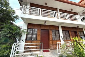 Un bâtiment à deux étages doté d’un balcon, de portes en bois et d’un petit espace porche.