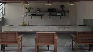 Un área de cocina con encimera de concreto, sillas de madera y estantes con electrodomésticos.
