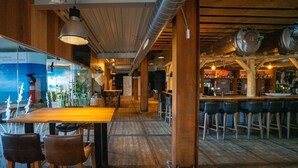 Een bar met houten tafels en stoelen, een bar en uitzicht op buiten.