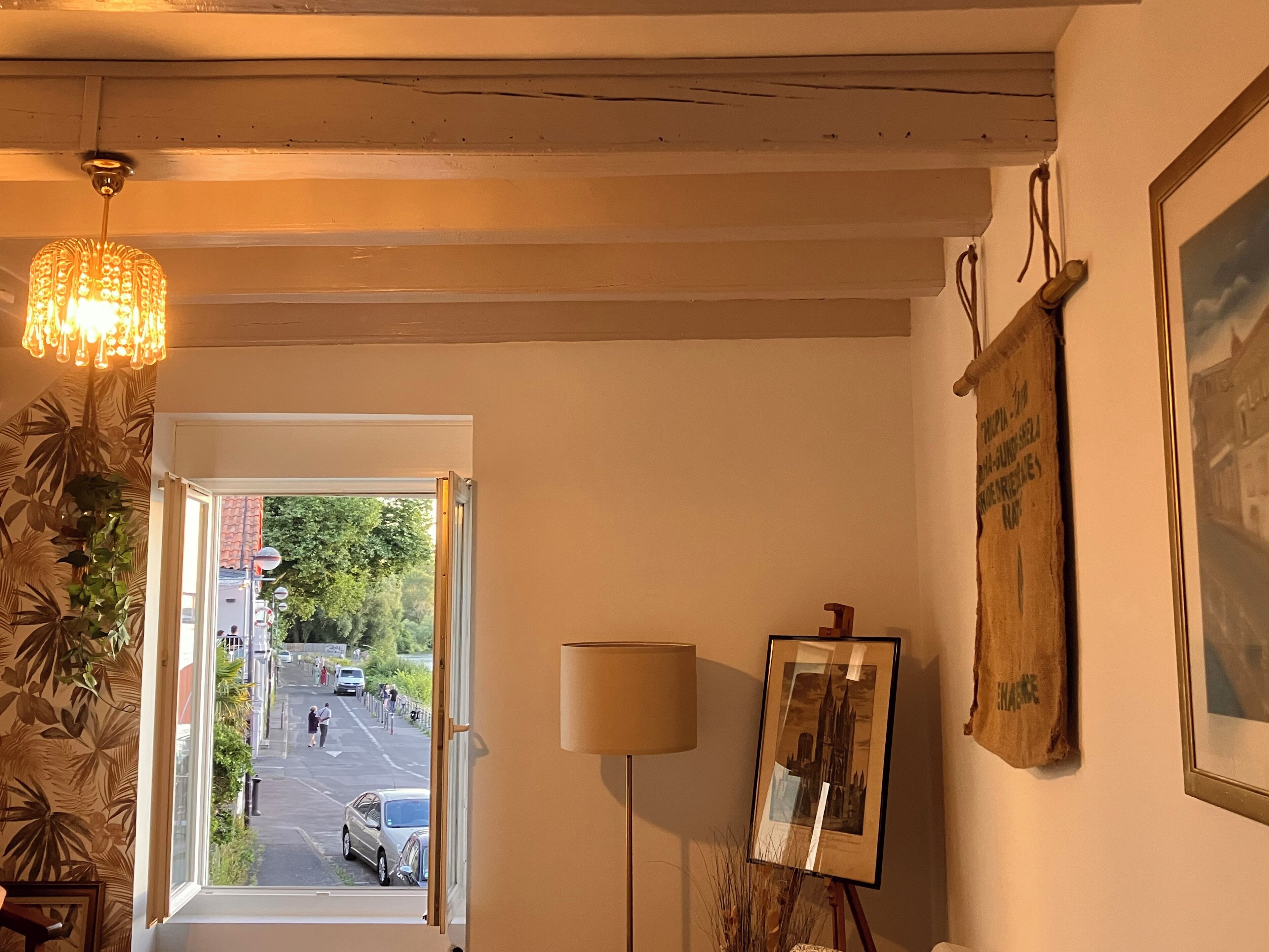 A room with a view of the street outside, a chandelier, a lamp, and a framed picture on the wall.