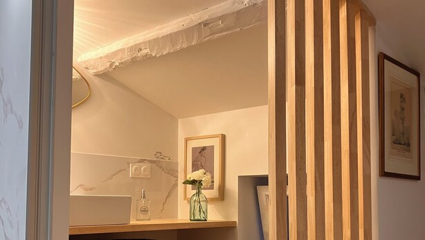 Une pièce avec une cloison en lattes de bois, un mur en marbre, une étagère avec des paniers, un tableau encadré et un tapis rouge.