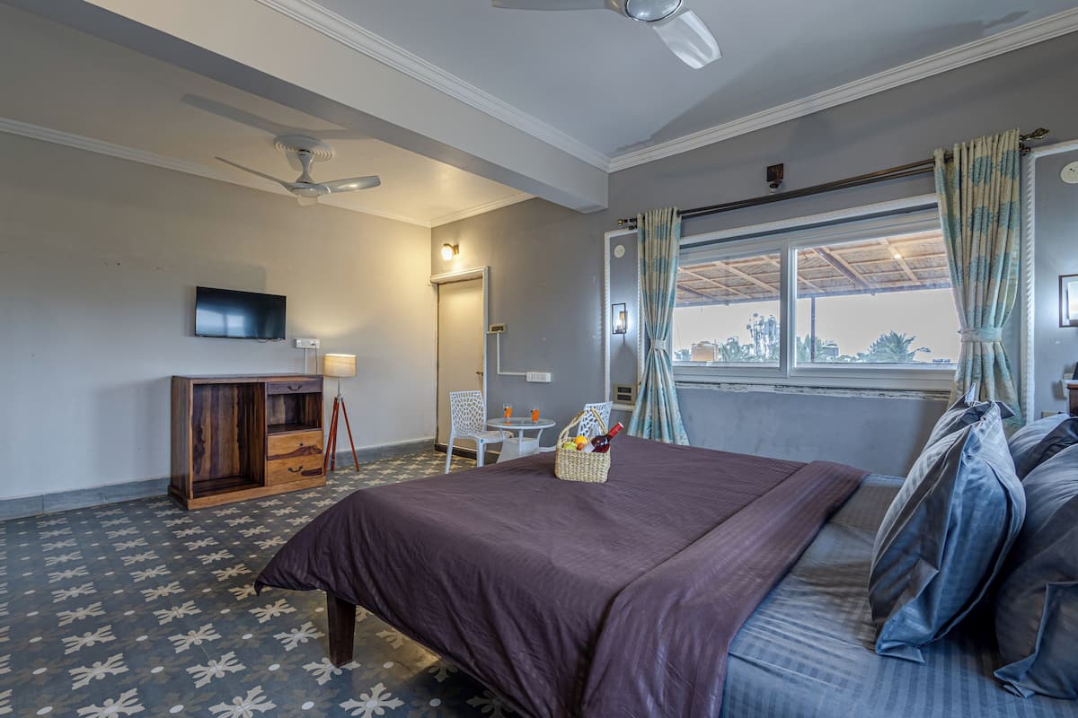 A bedroom with a bed, a TV, a desk, and a window with curtains.