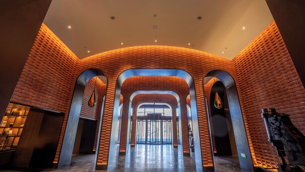 Een ruime lobby met een modern design, met bakstenen muren, grote gewelfde deuropeningen en een centraal open gebied dat leidt naar een lichte uitgang.