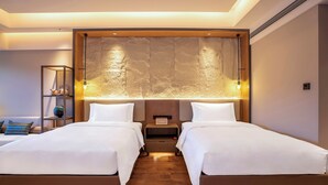 Hotelkamer met twee bedden, een nachtkastje, een plank met decoratieve objecten en een wandpaneel met structuur.