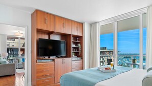Una habitación de hotel moderna con una cama grande, televisión, armarios de madera y un balcón con vista a la ciudad.